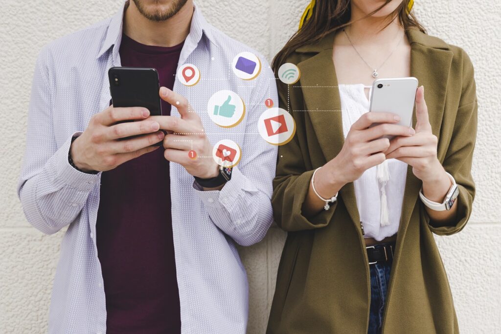 Duas pessoas, um homem e uma mulher, de pé mexendo no celular